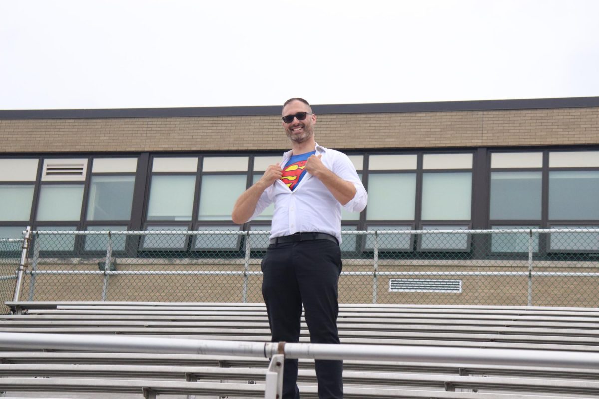 English teacher, Nicholas Emmanuele, poses with his Superman T-shirt in the Gus Anderson stands, at the 2024 Homecoming pep rally.